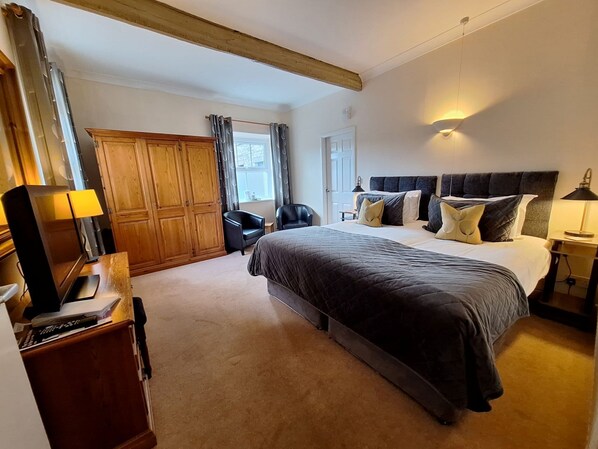 Een slaapkamer met een groot bed, een kledingkast, een bureau met lamp en een stoel.