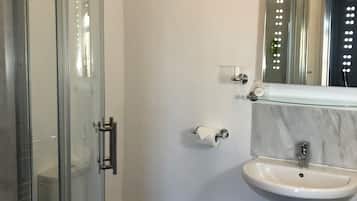 A modern bathroom with a glass shower enclosure, a white toilet, a marble sink, and a mirror with lights.