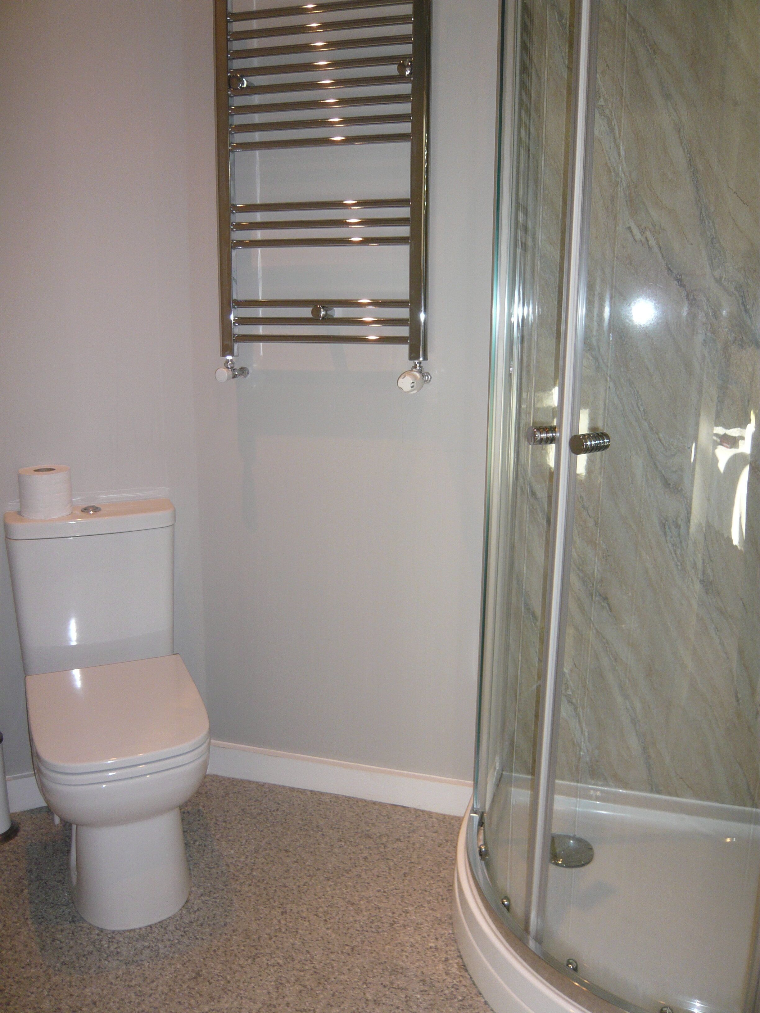 Un baño con inodoro, cabina de ducha de vidrio y pared de mármol.