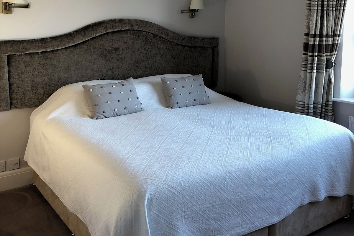 A neatly made bed with a white duvet, two pillows, and a headboard. There are two wall-mounted lamps on either side of the bed.