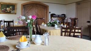 A dining room with a wooden door, a painting on the wall, and a table set with a vase of flowers, a teapot, and a sugar dispenser. - Pickmere Country House (Knutsford)