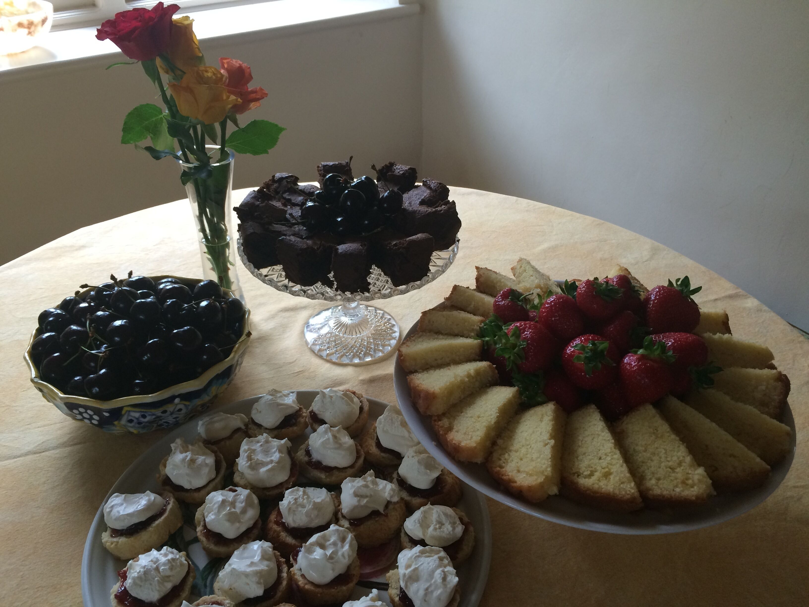 Una mesa con diversos postres, incluyendo un pastel con fresas, un bol de cerezas y un plato de scones con crema batida.
