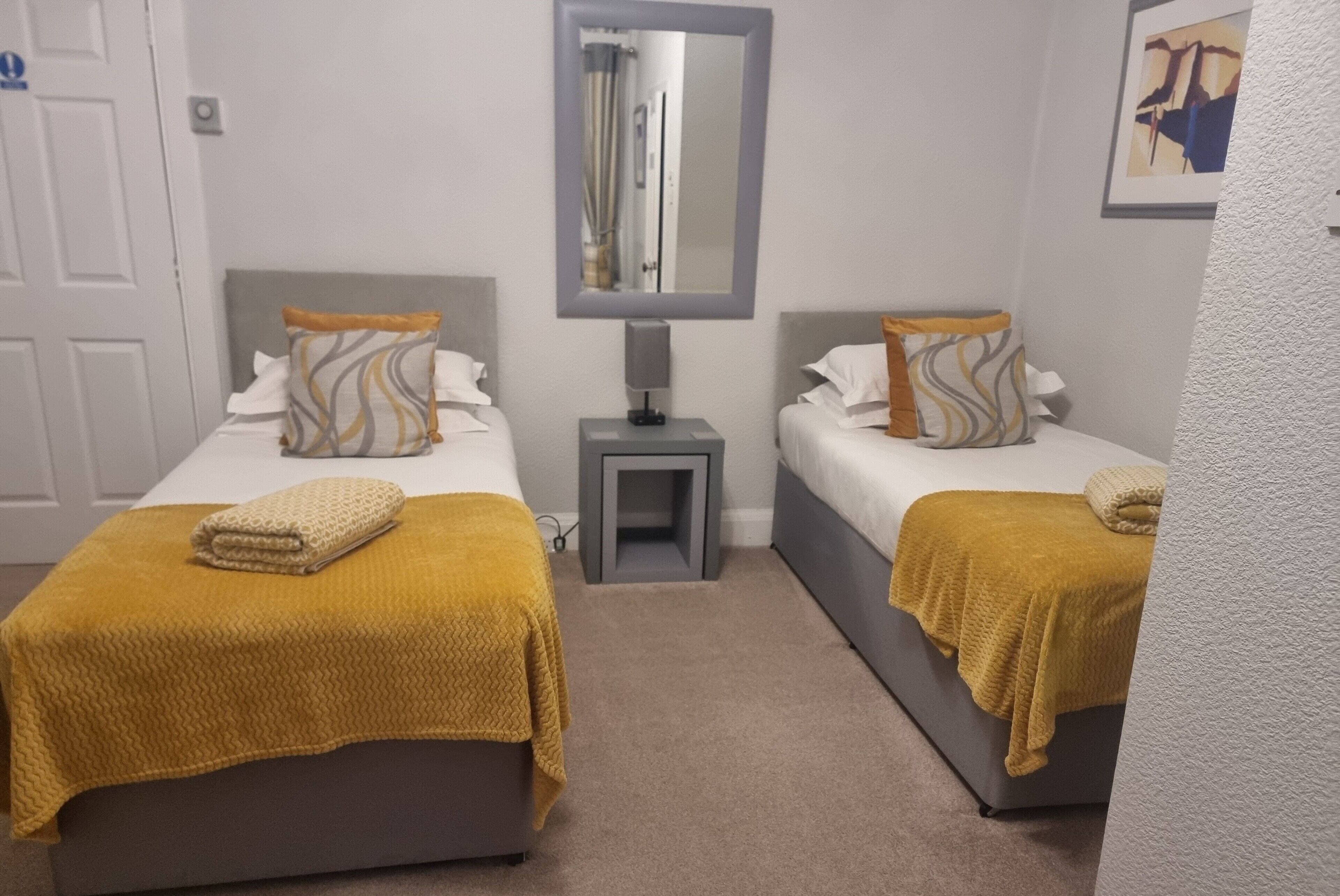 A hotel room with two beds, each with a headboard, a nightstand, a mirror, and a framed picture on the wall.
