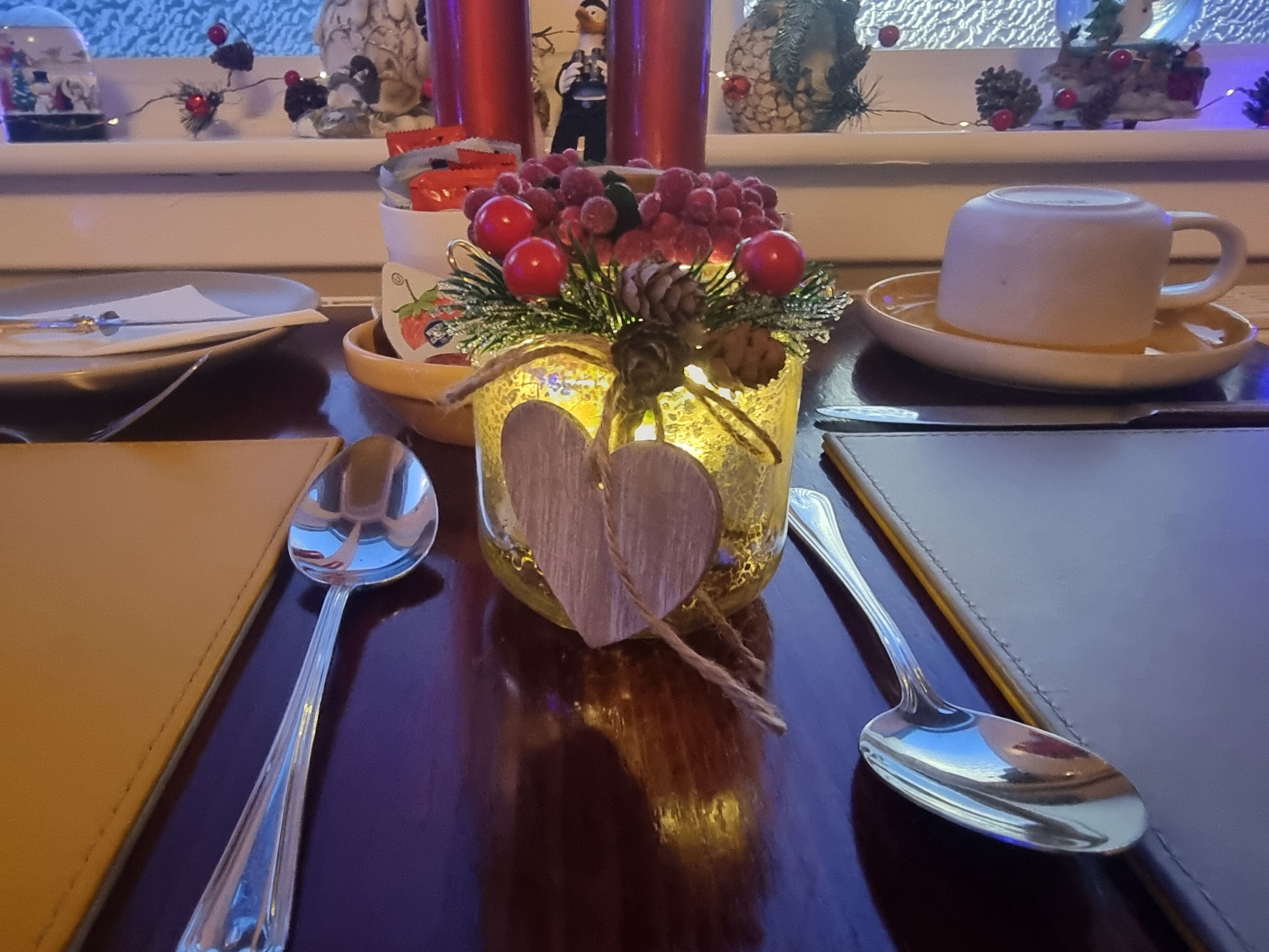 A table with a decorative centerpiece featuring a heart-shaped ornament, a glass vase with red berries, and a candle.