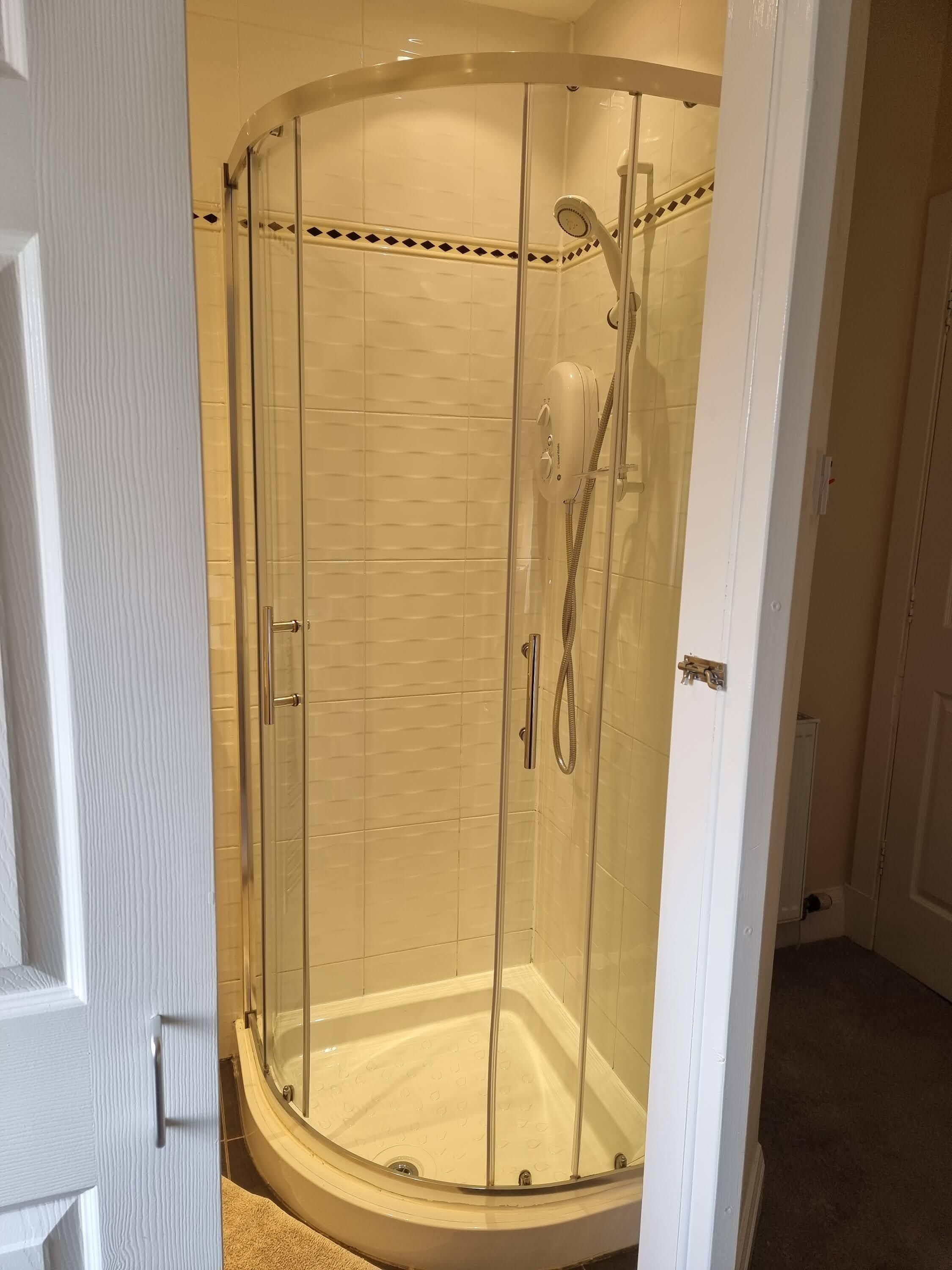 A glass-enclosed shower with a handheld showerhead and a handheld faucet.