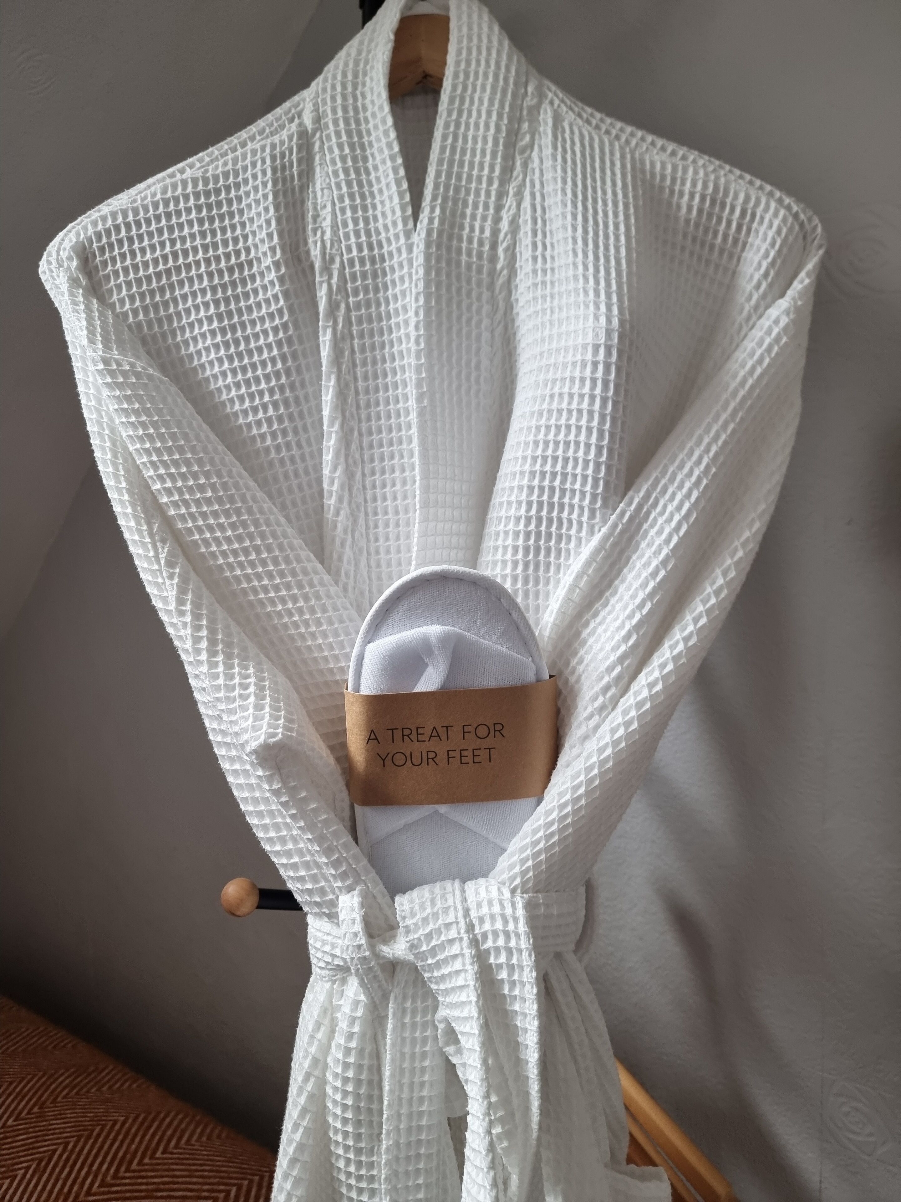 Un banyer blanc amb una etiqueta que diu 'Un regal per als teus peus' penjat en una perxa de fusta.