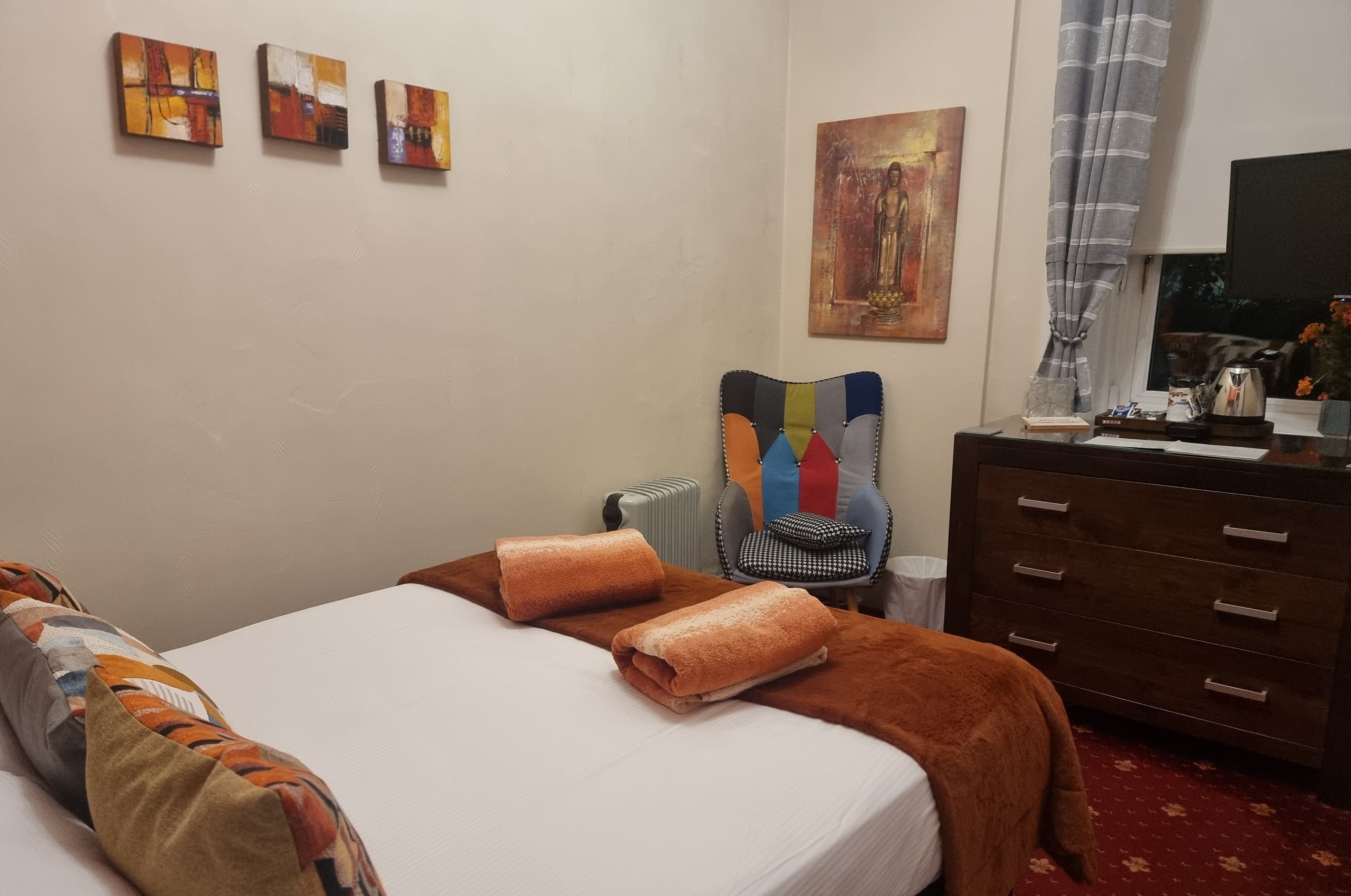 A hotel room with a bed, a chair, a dresser, and artwork on the walls.