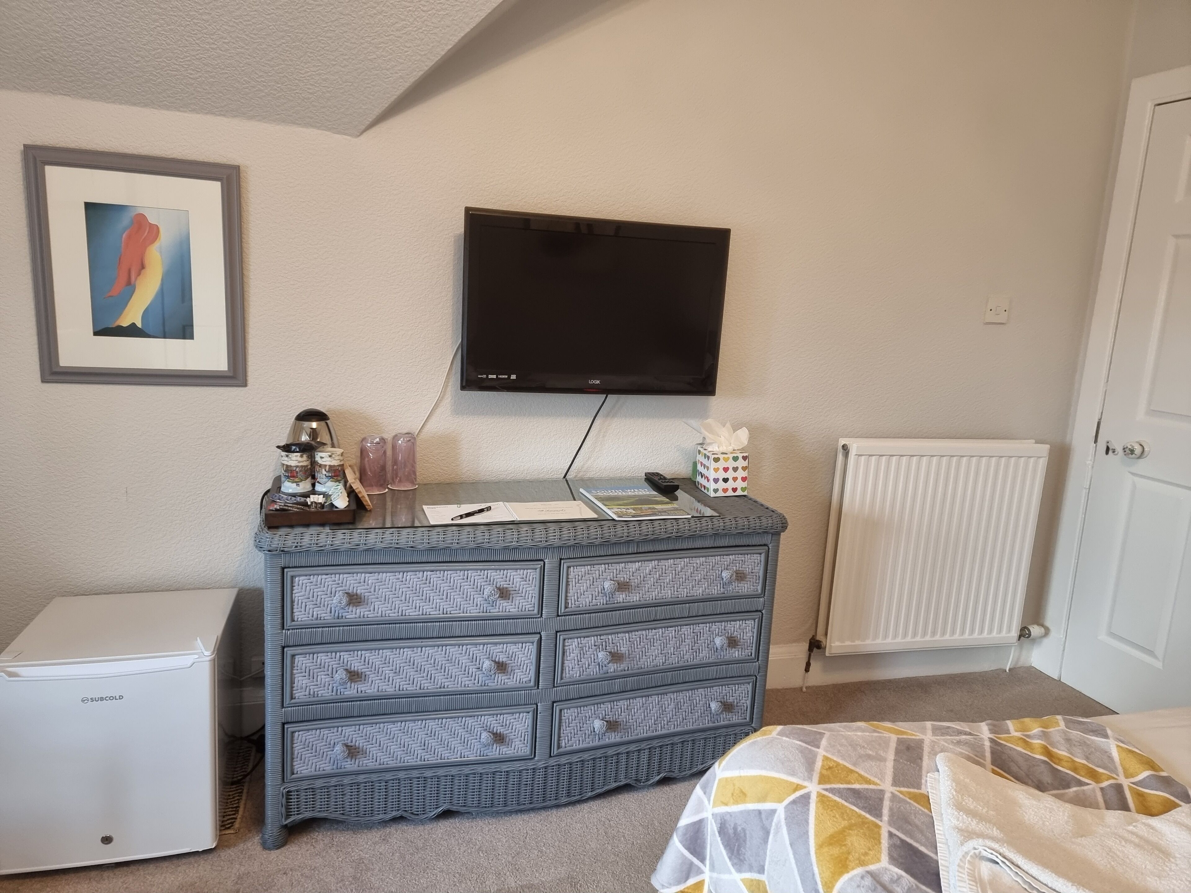 Un dormitorio con cama, cómoda, televisor y radiador.