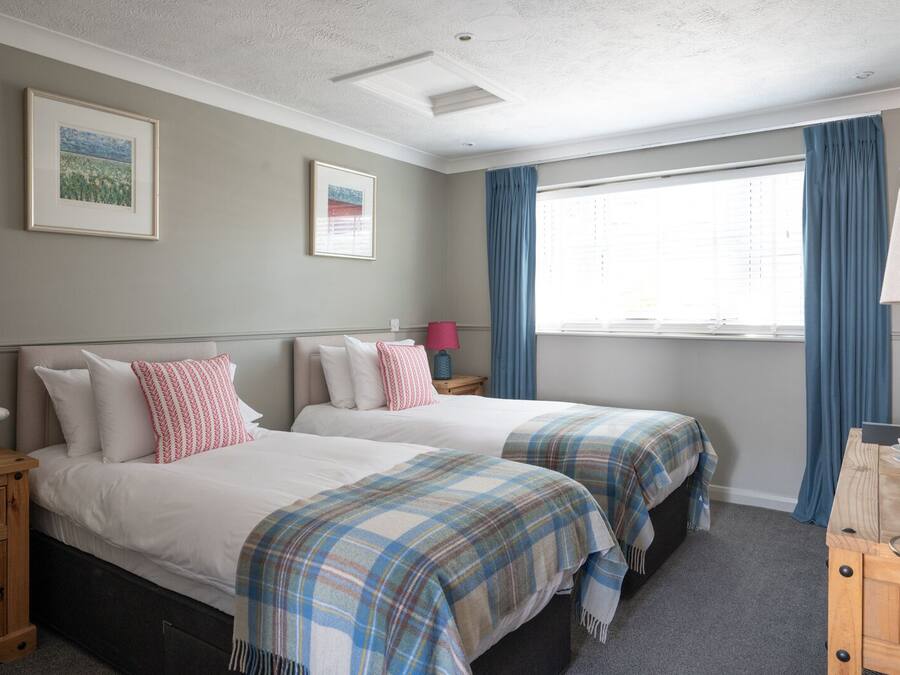 A hotel room with two beds, a wooden nightstand, a desk with a lamp, and a window with curtains.