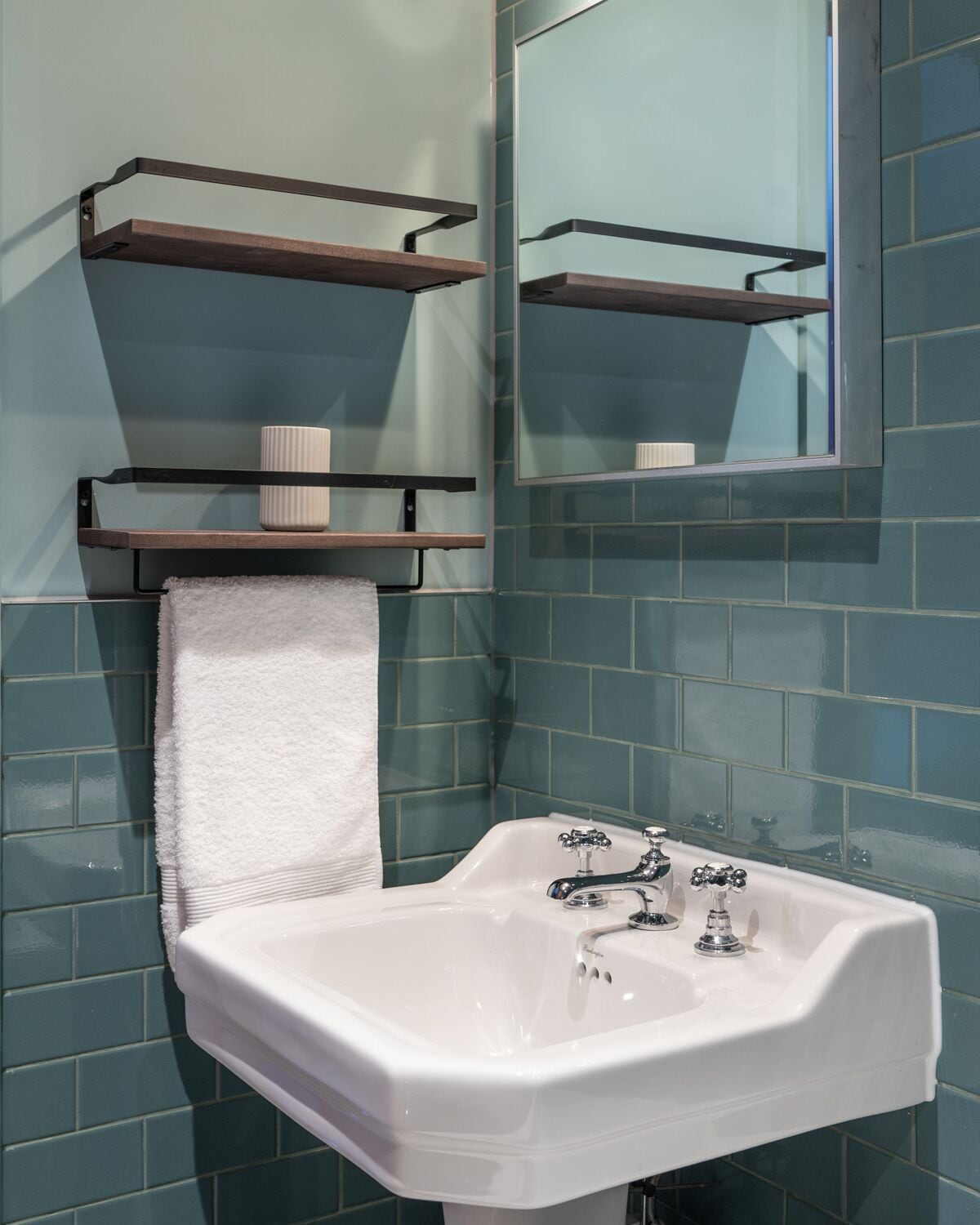 A bathroom with a white sink, two shelves above it, and a mirror on the wall.