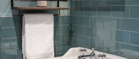 A bathroom with a white sink, two shelves above it, and a mirror on the wall.