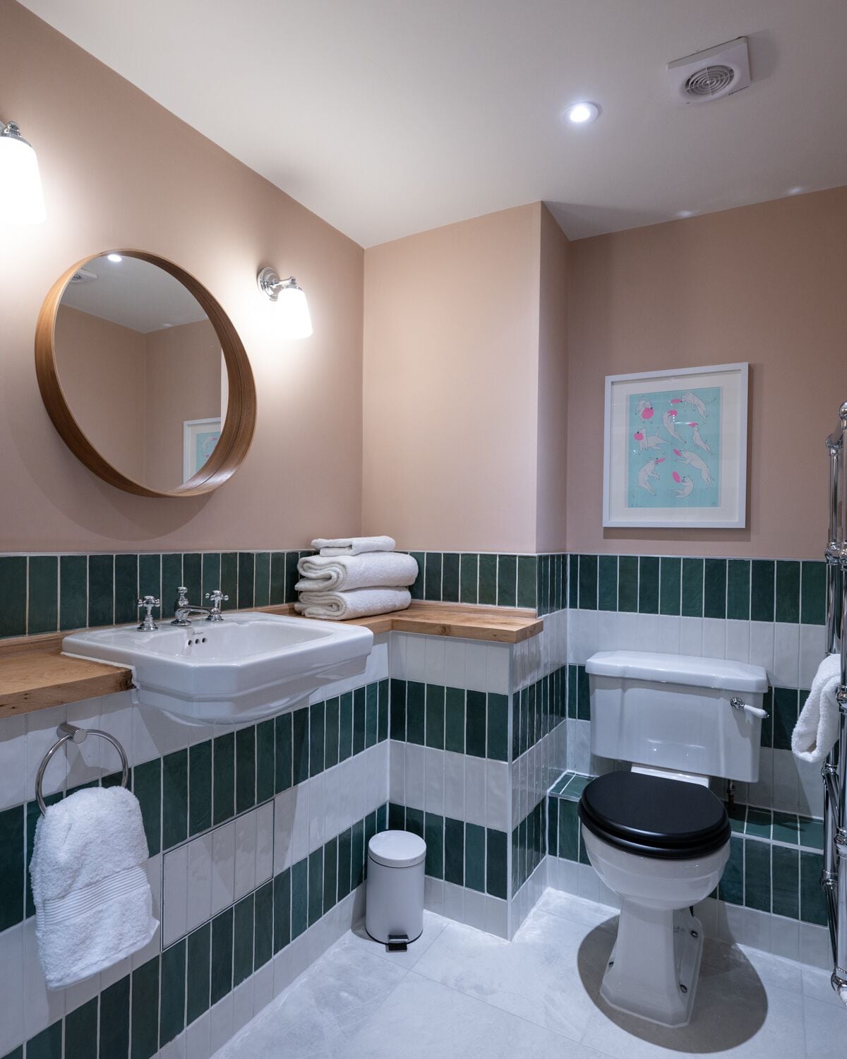 A bathroom with a sink, toilet, and mirror. There are towels stacked on the sink and a framed picture on the wall.