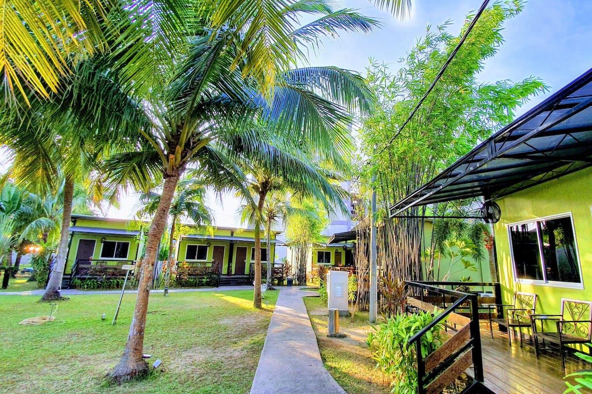 A resort with a covered outdoor seating area, palm trees, and a pathway leading to the buildings.