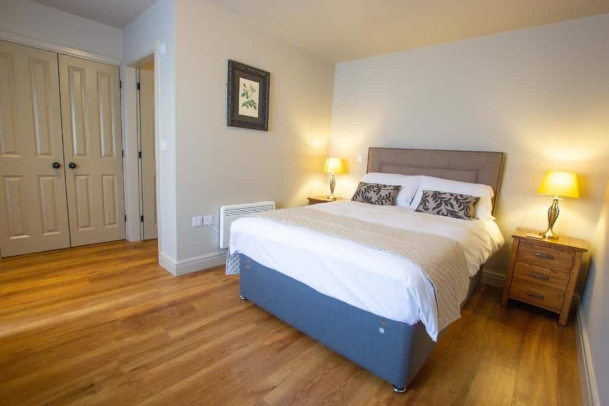 A bedroom with a bed, bedside lamps, a heater, and a door.