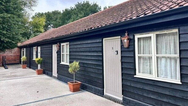 A row of dark wooden cottages with white trim, potted plants, and a clear sky. - The Cherry Tree Rochford (Rochford)