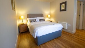 A bedroom with a bed, bedside lamps, a heater, and a framed picture on the wall. - The Cherry Tree Rochford (Rochford)