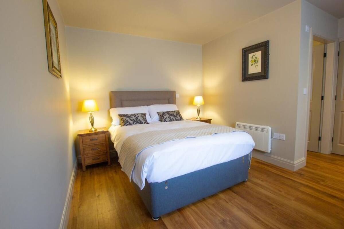 A bedroom with a bed, bedside lamps, a heater, and a framed picture on the wall.