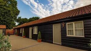 A row of log cabin-style buildings with a tiled roof, potted plants, and a clear sky. - The Cherry Tree Rochford (Rochford)