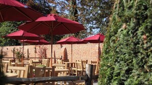Outdoor seating with red umbrellas, wooden tables, and chairs, with a brick wall in the background. - The Cherry Tree Rochford (Rochford)