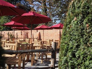 Outdoor seating with red umbrellas, wooden tables, and chairs, with a brick wall in the background.