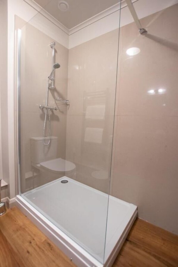 Zona de ducha con paredes de vidrio, base blanca y suelo de madera.