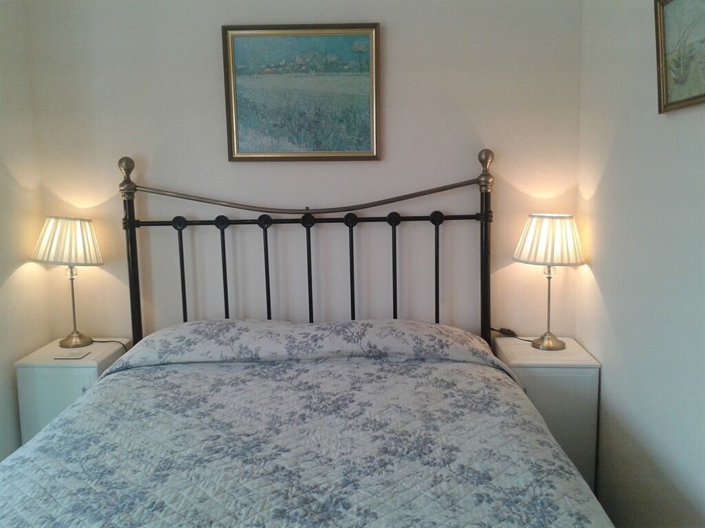 A bed with a floral bedspread, two bedside lamps, and a painting on the wall.