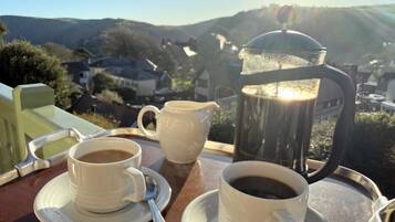 A tray with two cups of coffee and a coffee pot on a table with a view of a village.