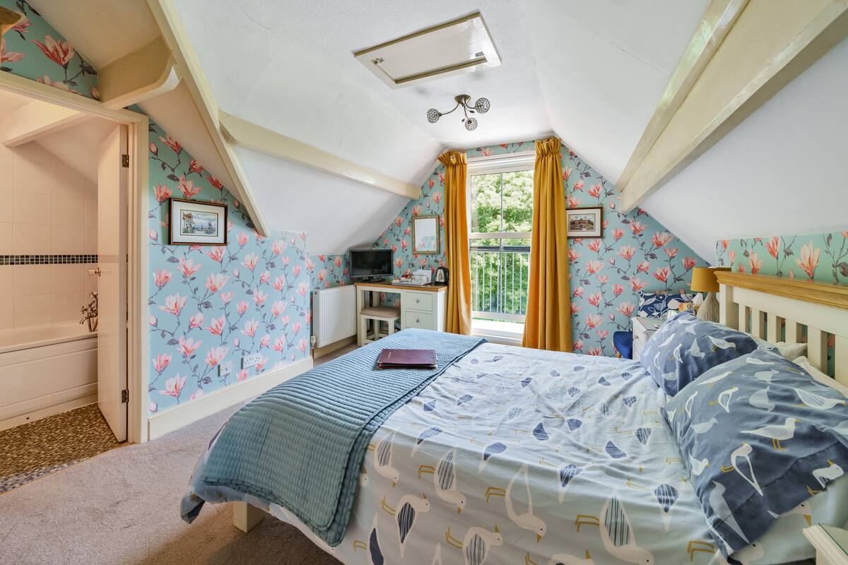 A bedroom with a bed, a desk, a television, and a window with curtains.