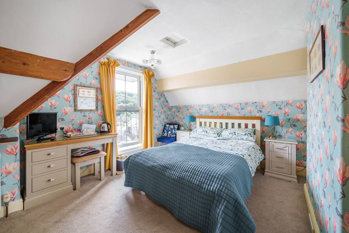 A bedroom with a bed, a desk, a chair, a television, and a window with curtains.
