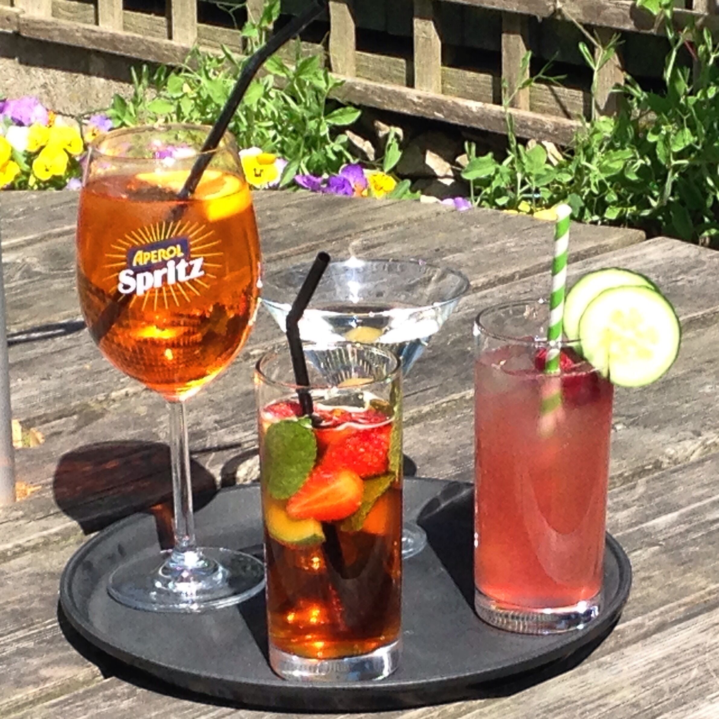 Three drinks on a wooden table with a garden background.