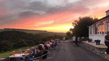 A sunset view from a terrace with outdoor seating, overlooking a valley.