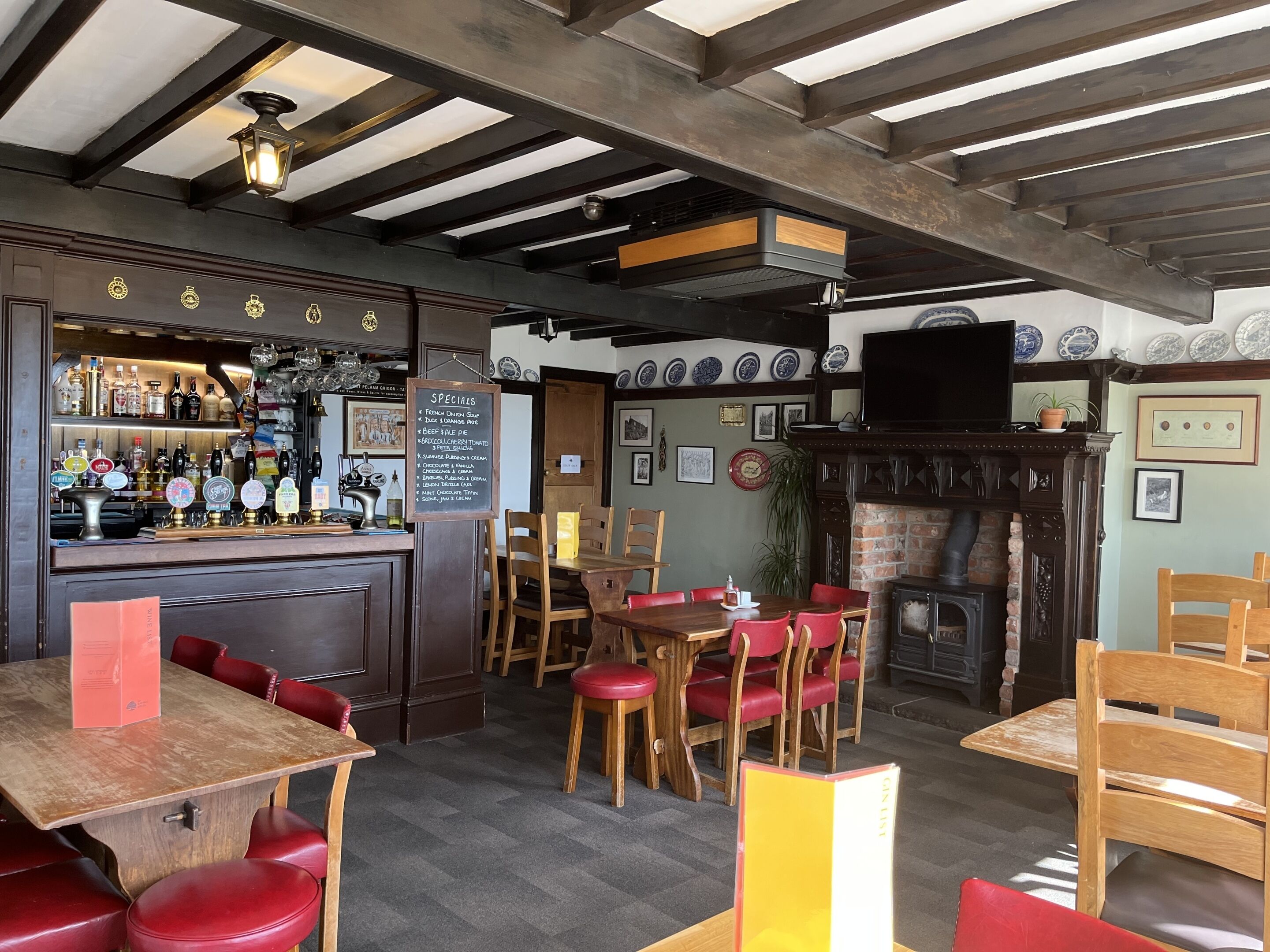 A cozy restaurant with wooden tables and red chairs, a bar area with various bottles, and a fireplace.