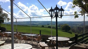 An outdoor patio with wooden tables and chairs, a black metal lamp post, and a view of a green landscape. - Lathkil Hotel (Bakewell)