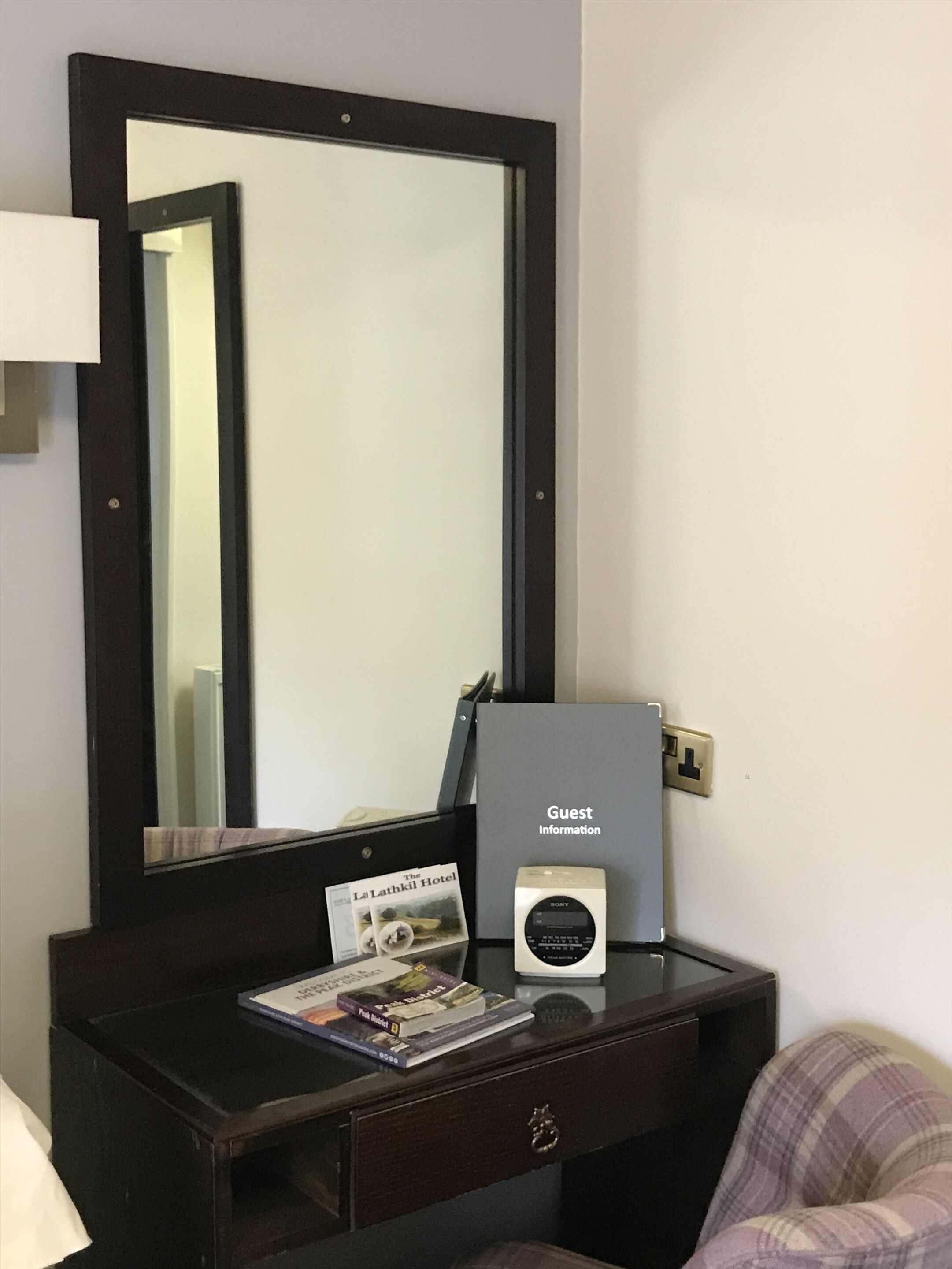 A hotel room with a large mirror, a bedside table with a Sony digital photo frame, a guest information card, and a brochure.