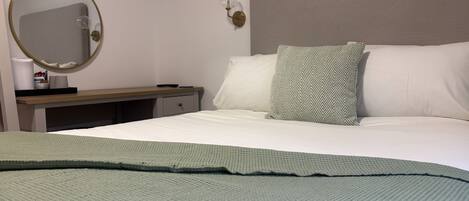 Una habitación de hotel con una cama, una mesita de noche, un espejo y una lámpara fijada a la pared.