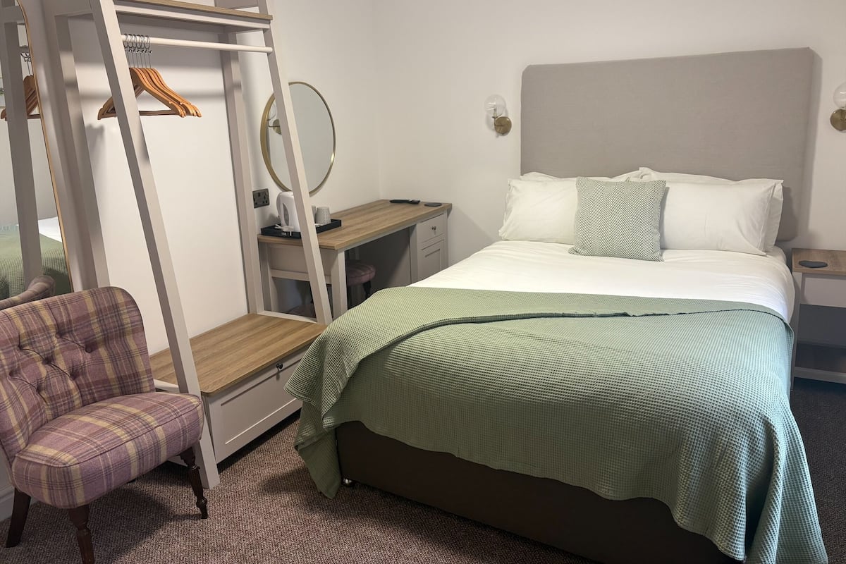 A bedroom with a bed, a chair, a desk, a mirror, and a wardrobe.
