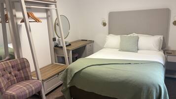 Een slaapkamer met een bed, een stoel, een bureau, een spiegel en een kledingkast.