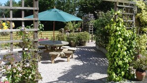 A garden patio with a wooden pergola, a green umbrella, and a table with benches. - Leworthy Farmhouse (Holsworthy)