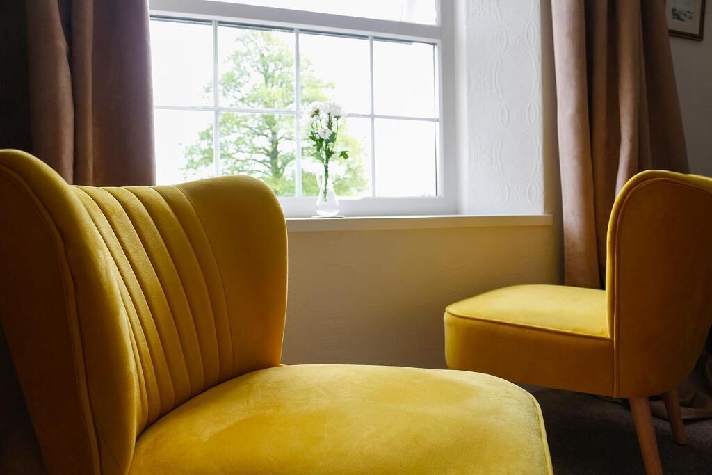 A room with two yellow chairs positioned near a window with a view of trees.