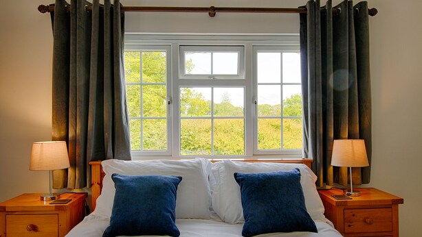 A bedroom with a large bed, two bedside tables, and a window with curtains. - Leworthy Farmhouse (Holsworthy)