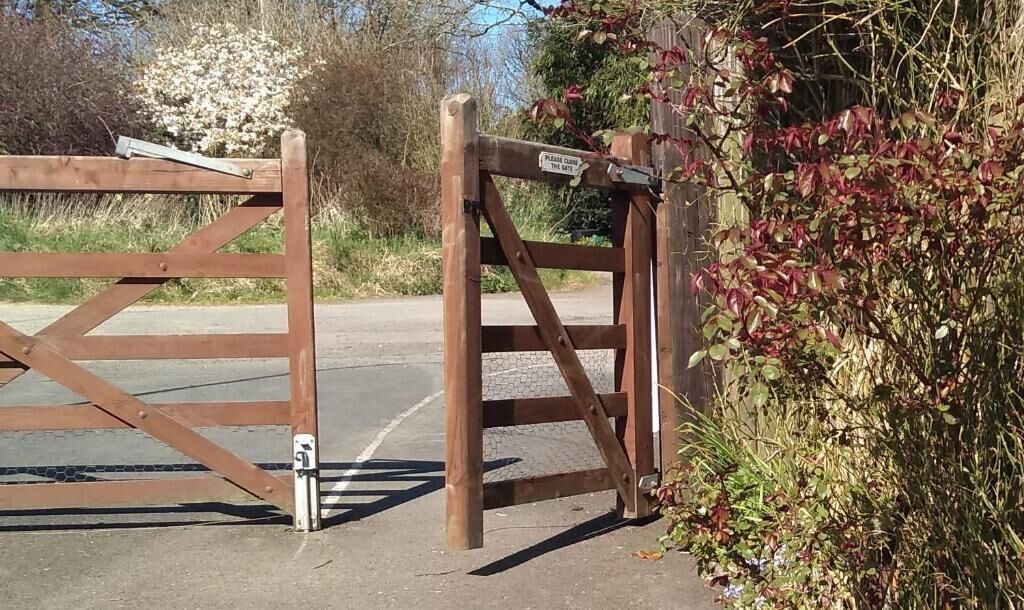 A wooden gate with a sign, a metal gate latch, and a paved road.