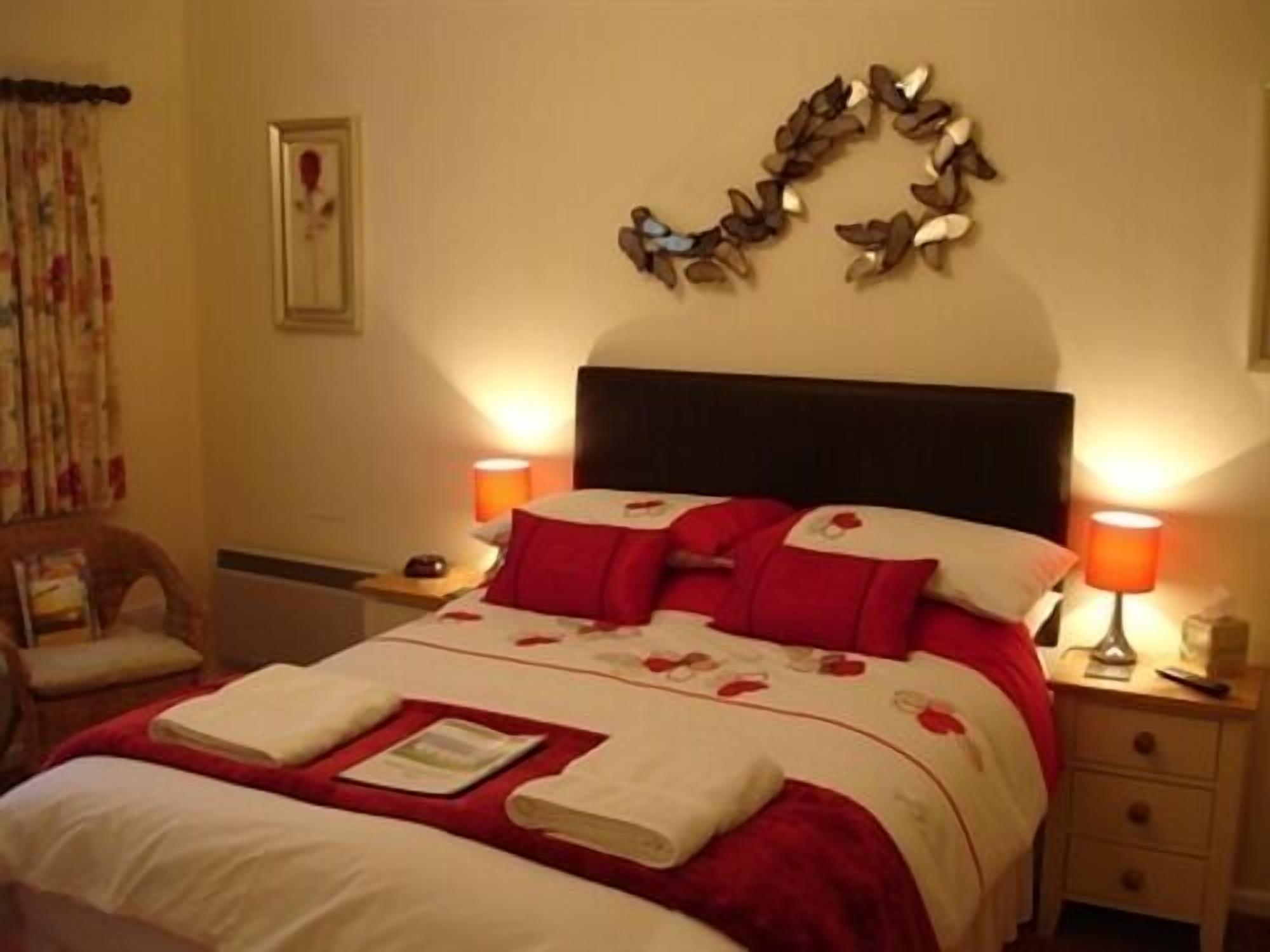 A neatly made bed with red and white bedding, two bedside lamps, and a wall decoration above the bed.