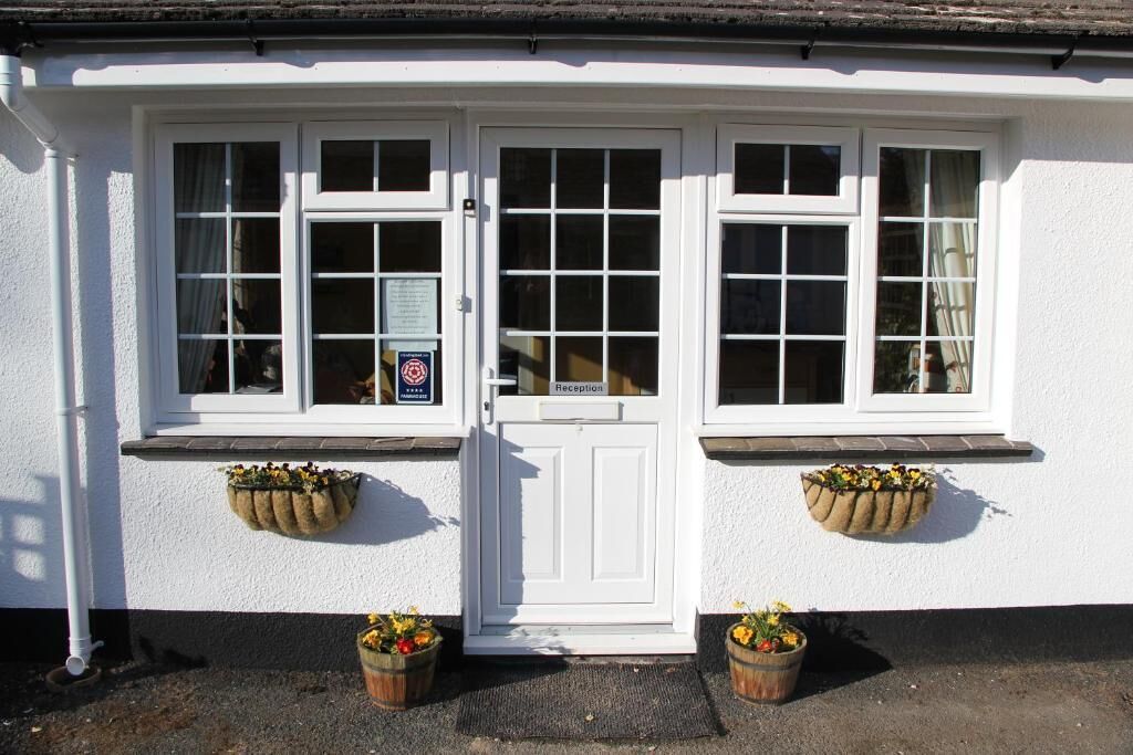 A white building with a reception door, two windows with curtains, and flower baskets on the windowsills.