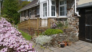A stone house with a wooden fence, a garden with flowers, and a black garage door. - Leworthy Farmhouse (Holsworthy)