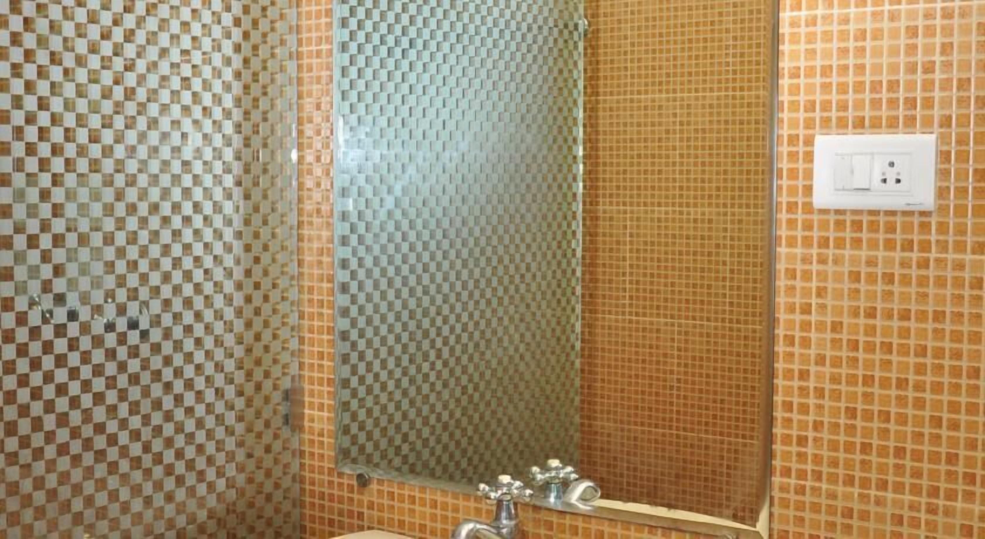 Une salle de bain avec des murs recouverts de carreaux disposés en motif à carreaux, une douche en verre et un miroir au-dessus du lavabo.