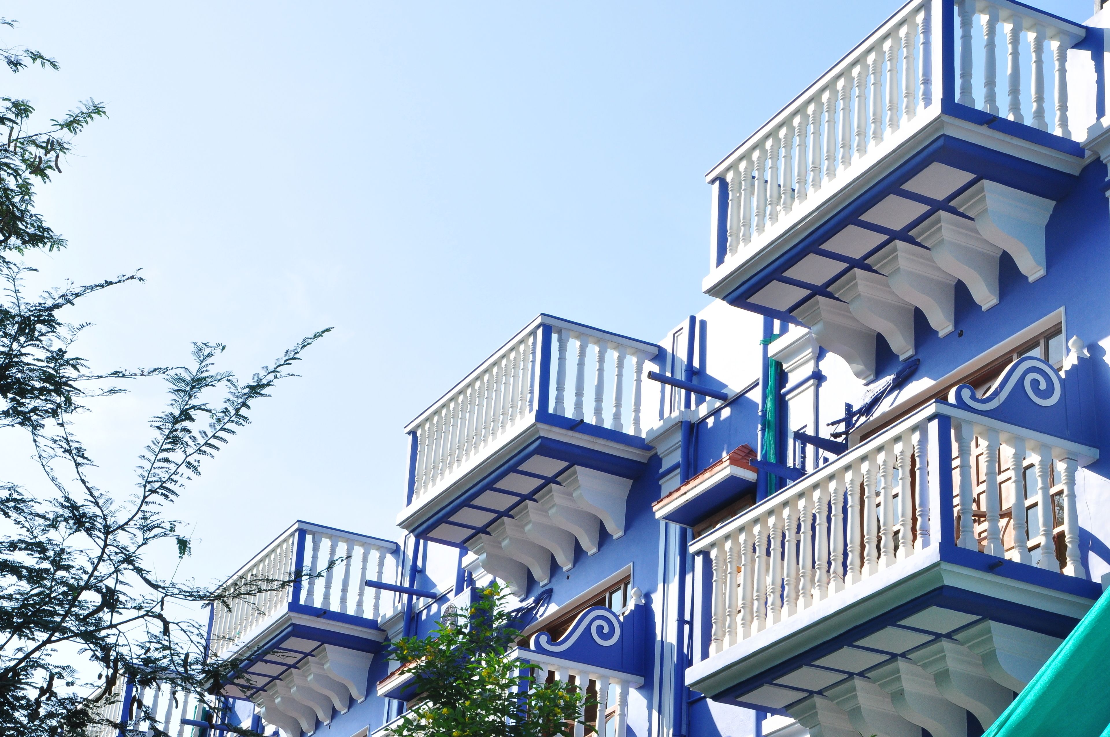 Un immeuble doté de nombreux balcons, de rampes blanches et, en arrière-plan, d’un ciel d’un bleu limpide.