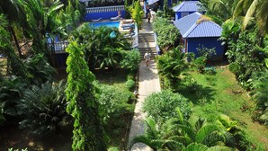 A pathway leading to a pool area surrounded by lush greenery and blue buildings.