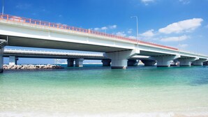 A bridge over clear turquoise water with a sandy beach in the foreground. - Comfort Inn Naha Tomari Port (Naha)