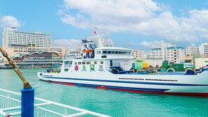A large white ferry with blue and red stripes, docked at a port with buildings in the background. - Comfort Inn Naha Tomari Port (Naha)