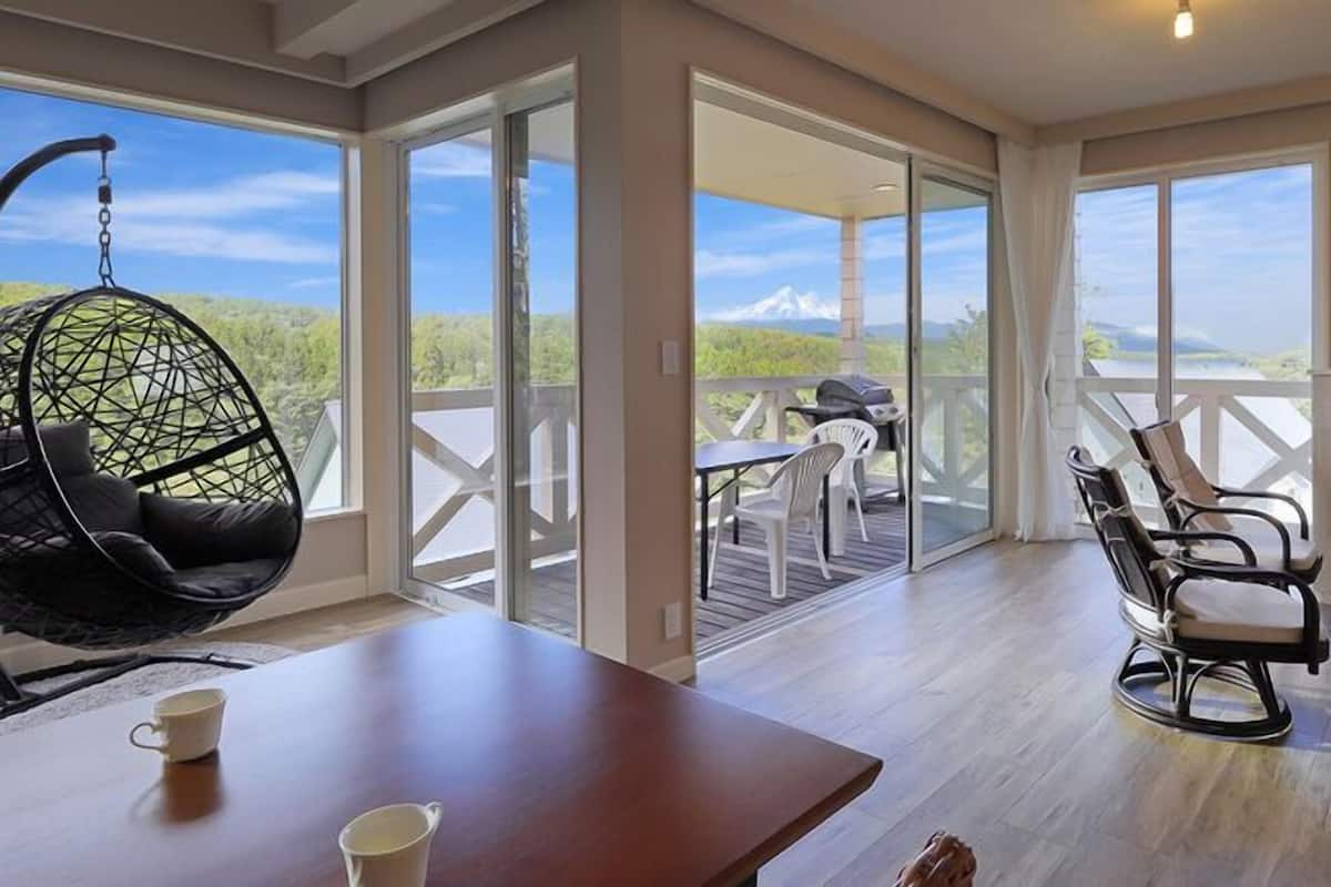 A spacious room with a large sliding glass door leading to an outdoor patio, a hanging chair, a TV, and a wooden table.